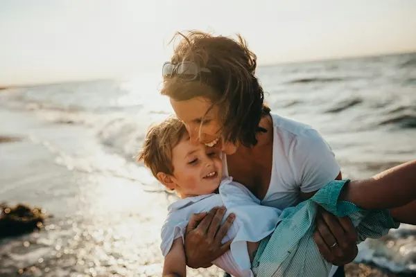 A mother laughing with her son at the water's edge