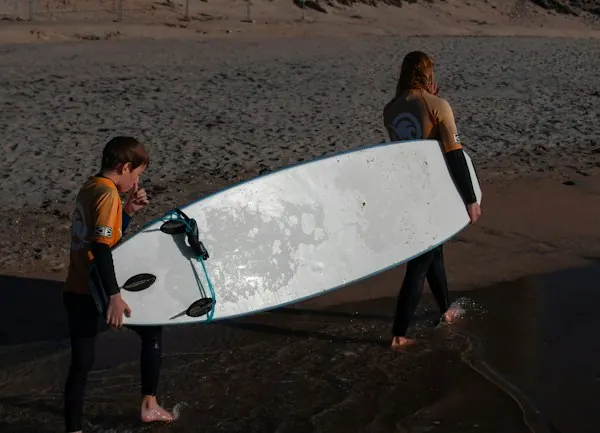 Two young surfers carrying a board up the beach