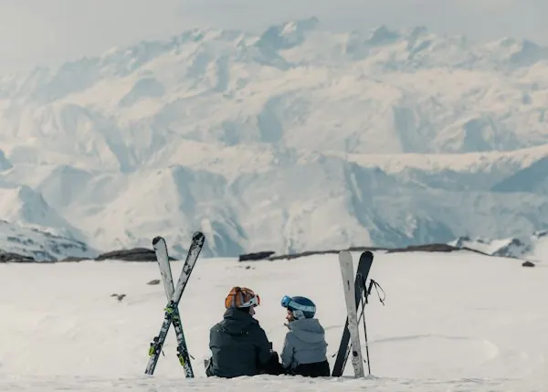 Two people resting beside their skis, facing the mountains